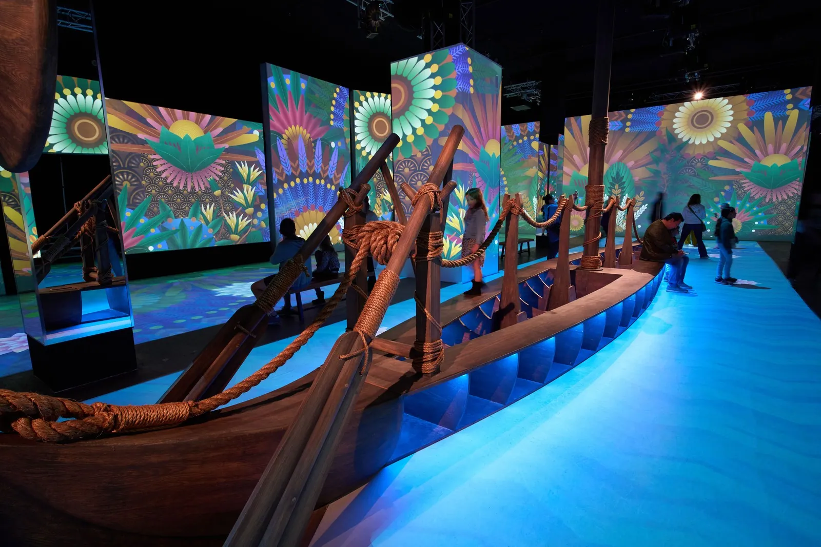 A projection-lit exhibition room with a wooden boat at Magic Box Event Campus