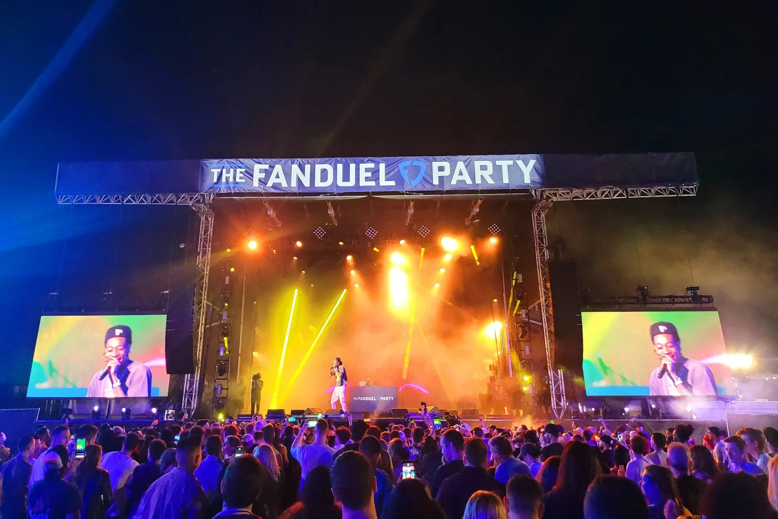 A crowd in front of a concert stage lit in yellow and orange