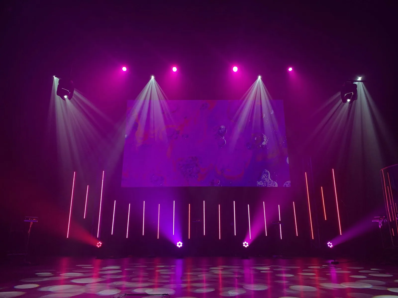 An empty stage washed in magenta light beams