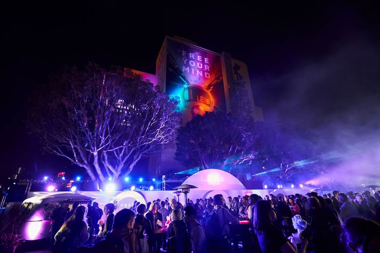 A crowd at a night event outside a building lit with a projected message